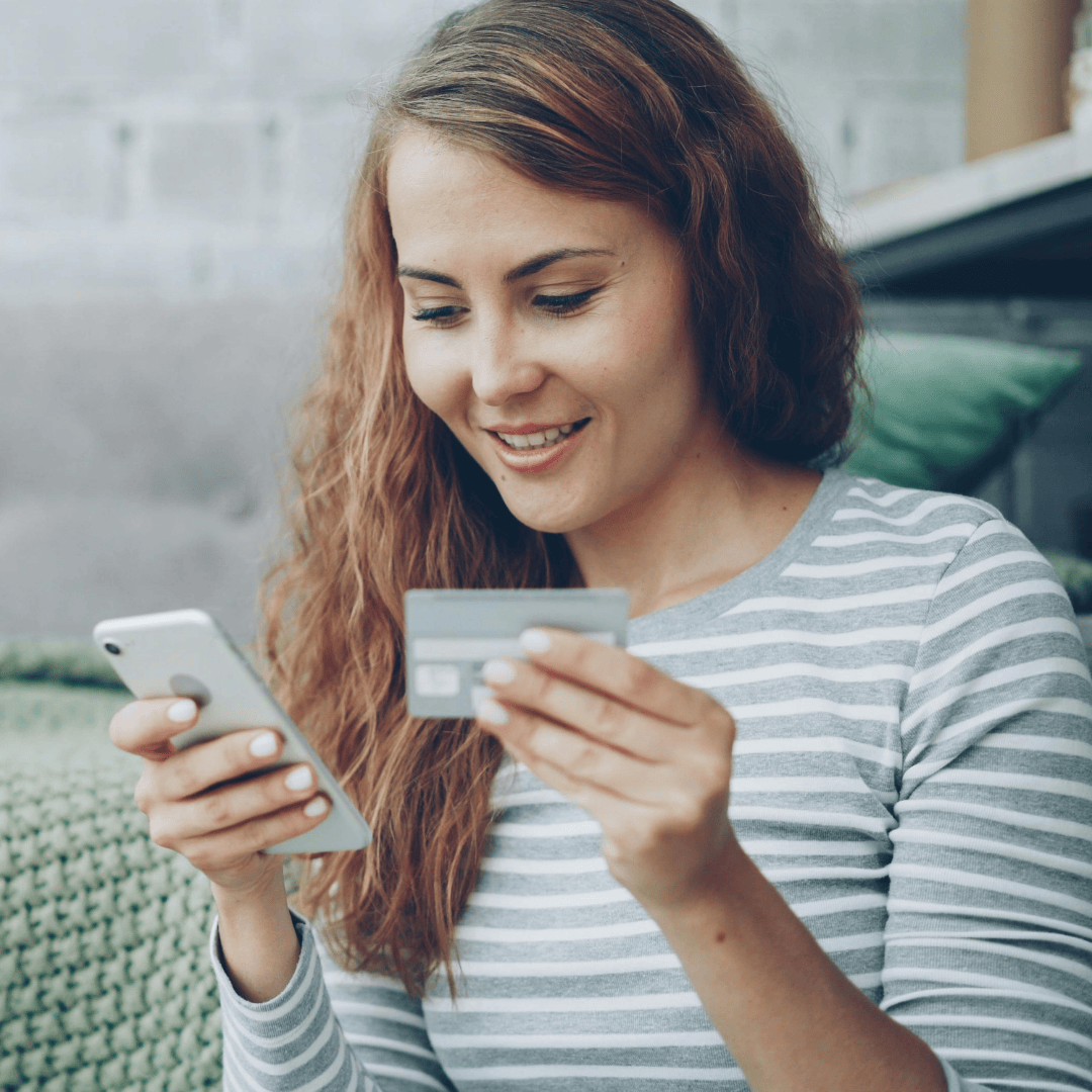A person holding a credit card and a smartphone, appearing to make an online purchase.
