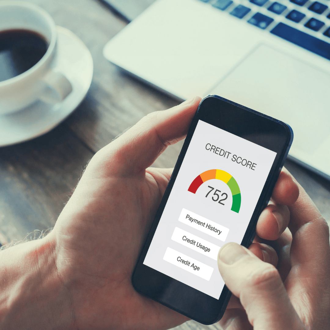 A person holds a smartphone displaying a credit score of 752 with categories for Payment History, Credit Usage, and Credit Age. A laptop and coffee cup are visible in the background.