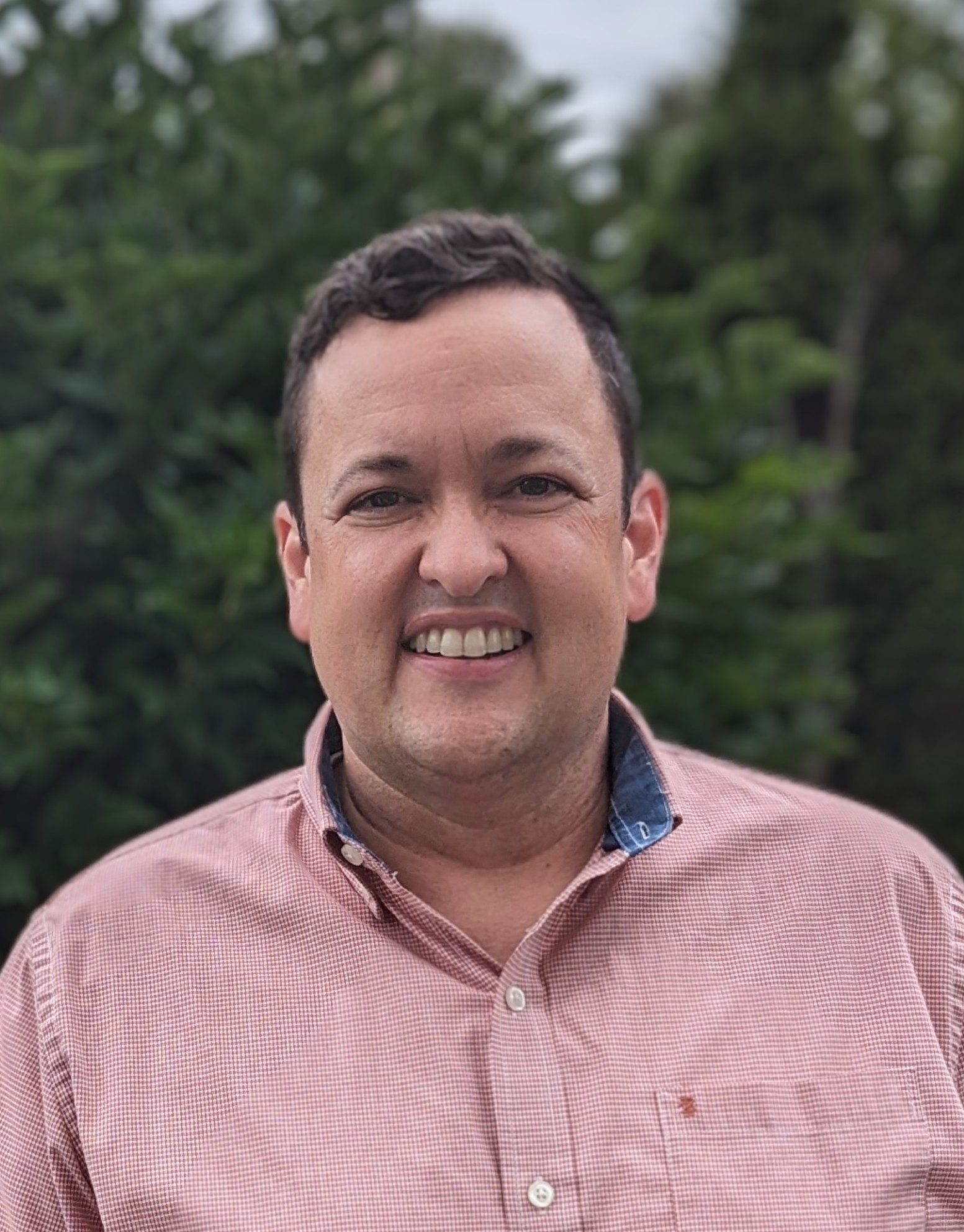 Headshot of Andrew McGeorge in portrait mode in front of bushes