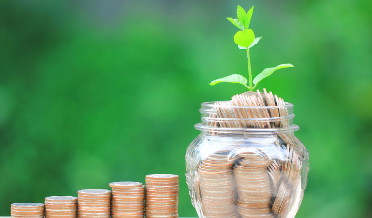 Graduated stacks of coins beside a glass jar full of coins with a plant sprouting from the top. Picture depicts a growing savings account.