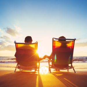 Individual Retirement Accounts. Couple sitting on a beach at sunset, holding hands.
