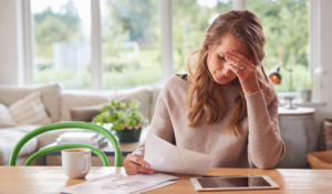 Ovedraft - Woman sitting at a table with her hand on her forehead while she looks at bank statements, indicating stress