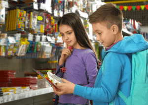 A school-age boy and girl standing in the school supply aisle looking at supplies.
